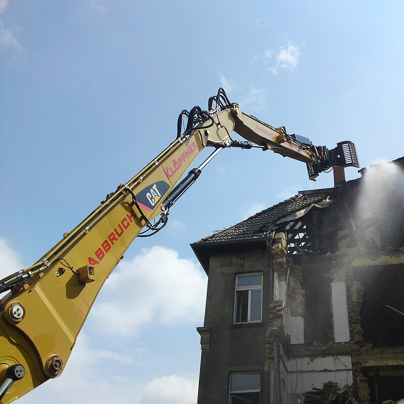 Baggerarm reißt das Dach eines Hauses ein