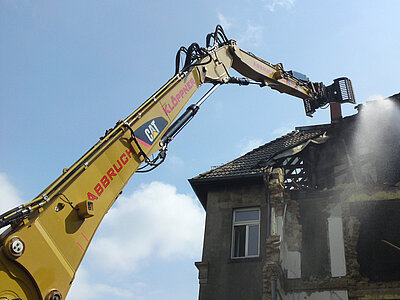 Baggerarm reißt das Dach eines Hauses ein
